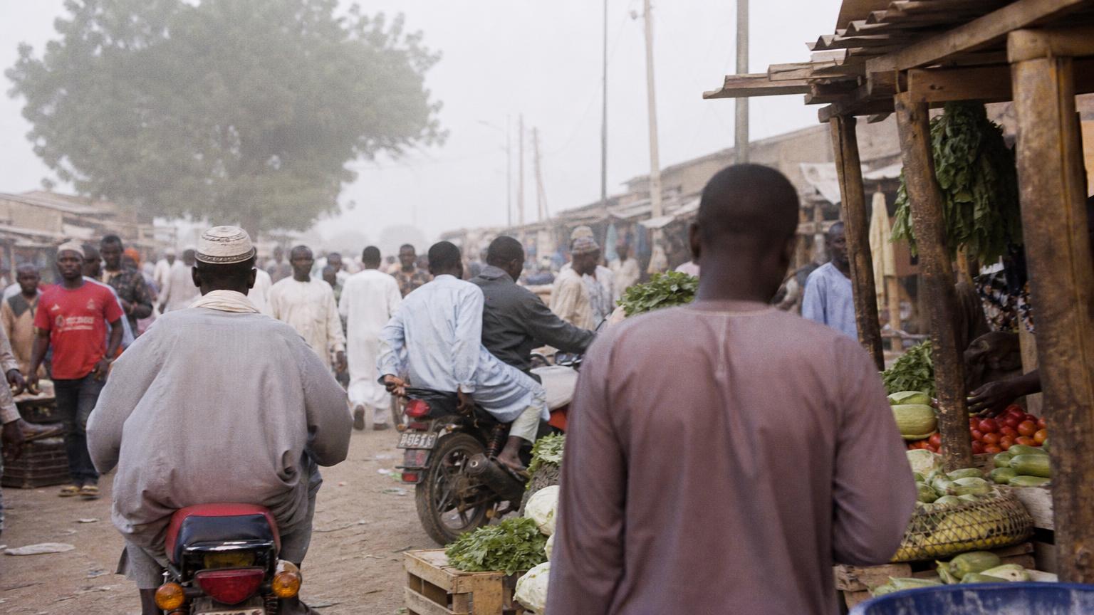 Rue du marché de Dembé au petit matin, motos, étals de légumes et passants